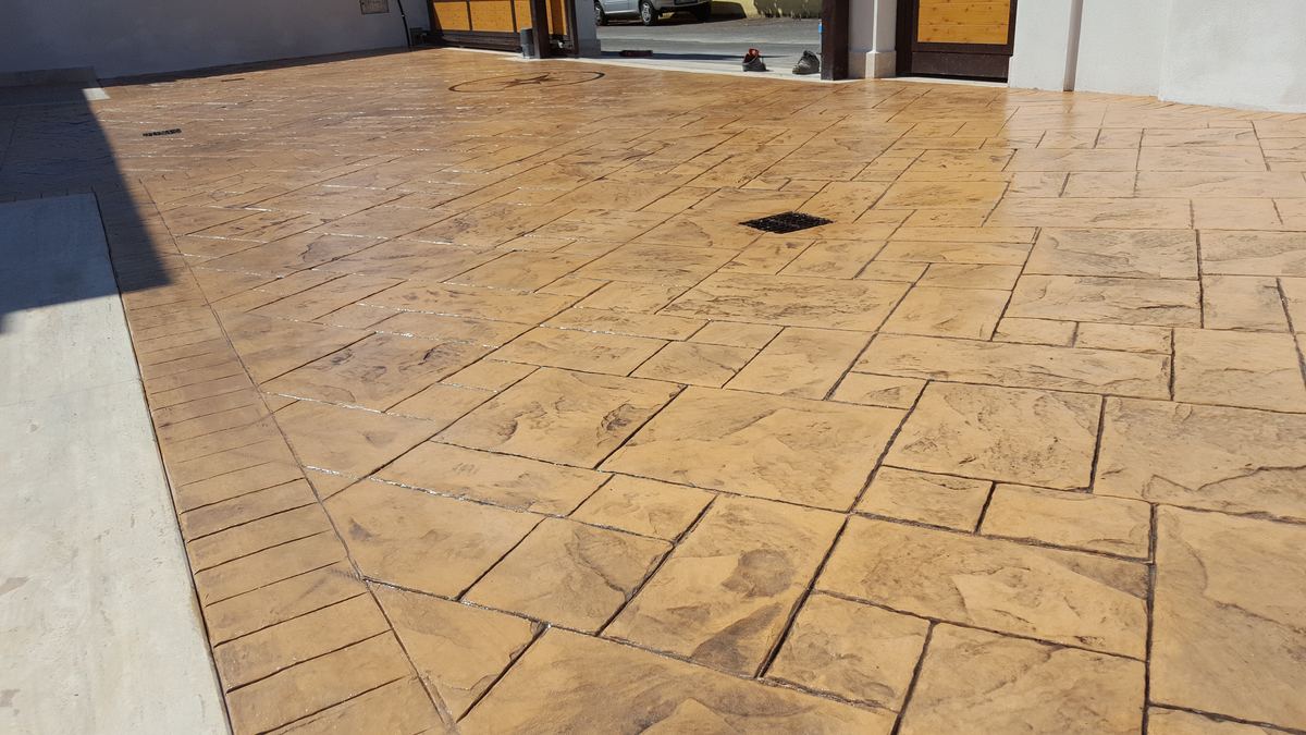 Finished sandstone-coloured ashlar pattern imprinted concrete driveway in front of a pair of garages